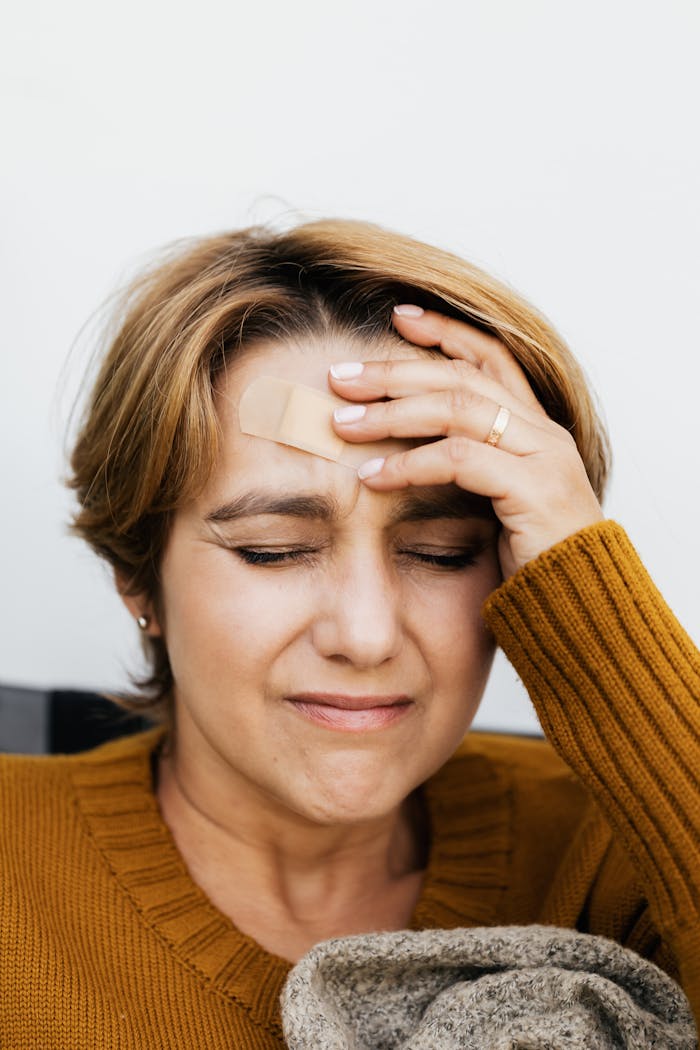 Close-up of a woman with a band aid on her forehead, eyes closed from pain