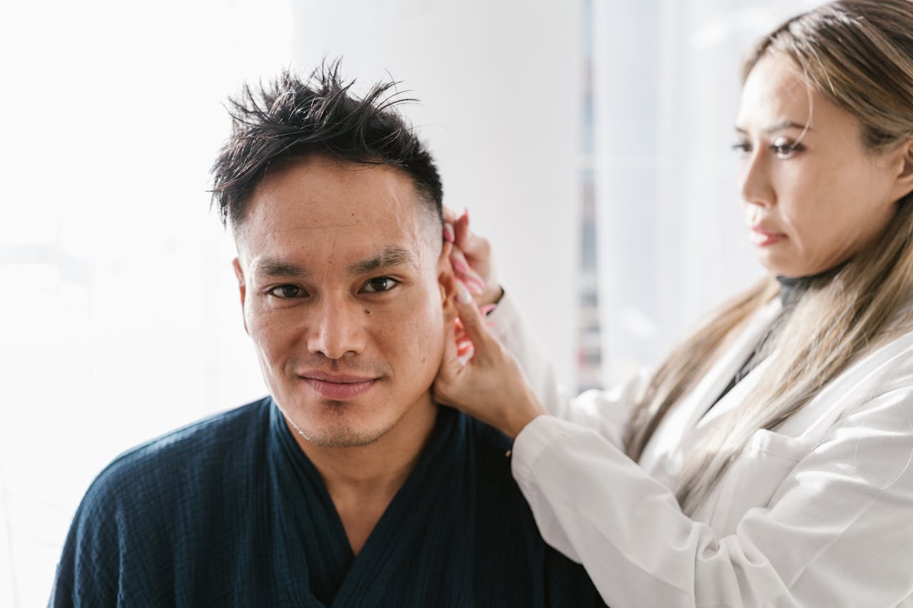 our-story A doctor performs an ear examination on a patient in a well-lit clinic setting.